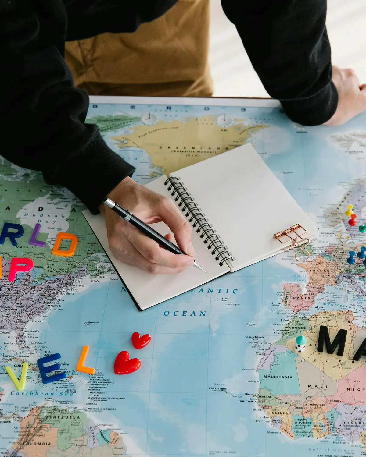 Persona escribiendo en cuaderno sobre mapamundi planeando viaje, Técnico Laboral en Agencia de Viajes Córdoba