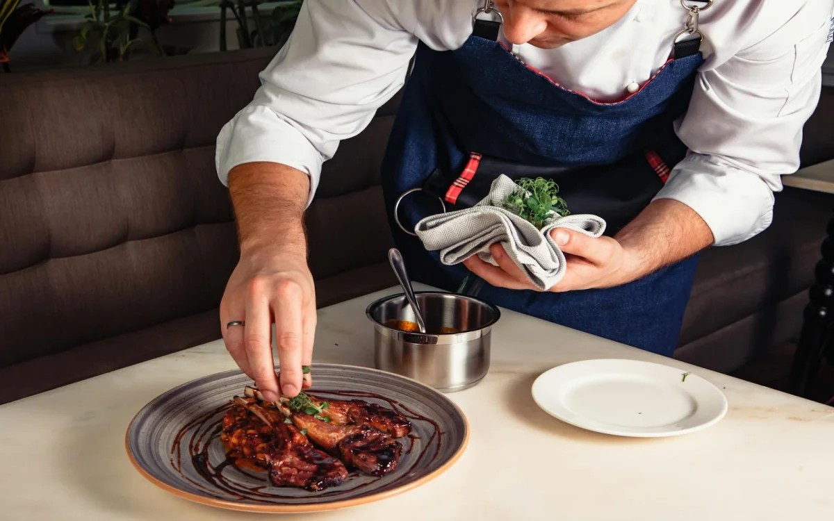 Chef emplatando un plato gourmet de cordero con precisión, especialización del programa Técnico Laboral en Cocina