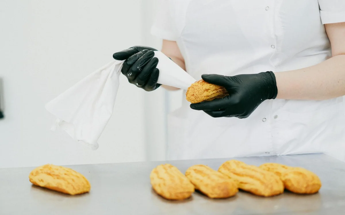 Chef pastelero aplicando crema a eclairs en panadería, etapa productiva del programa Técnico Laboral en Cocina Córdoba