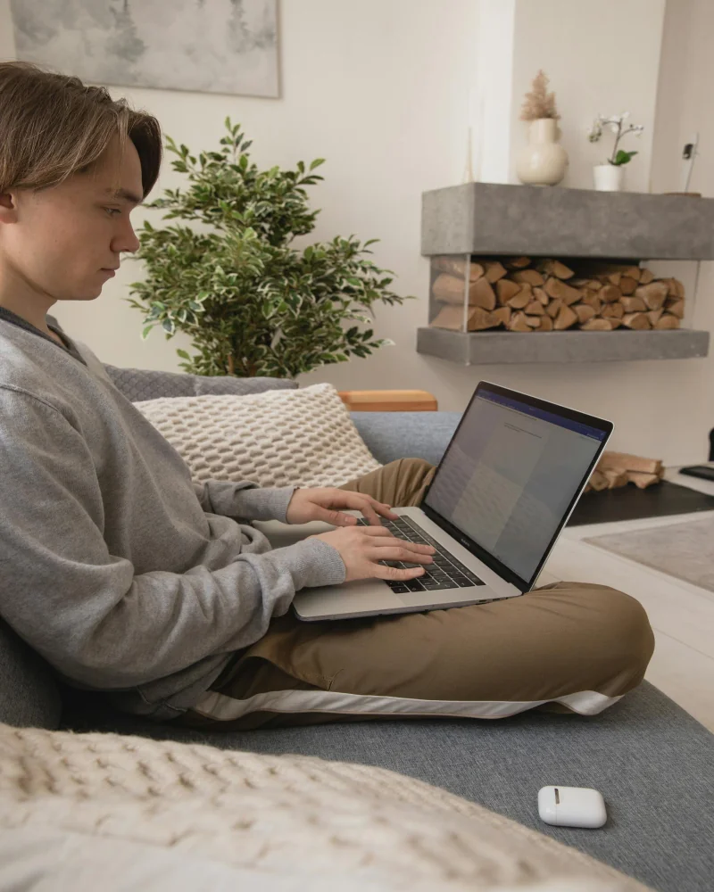 Joven con laptop en sofá, inscripción digital al programa Técnico Laboral en Cocina